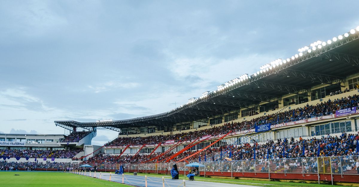 A packed stadium with enthusiastic spectators watching a live sports event under bright lights.