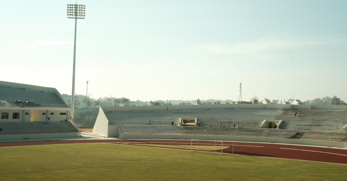 Explore an aerial view of a serene sports stadium with empty seating and a clear sky.