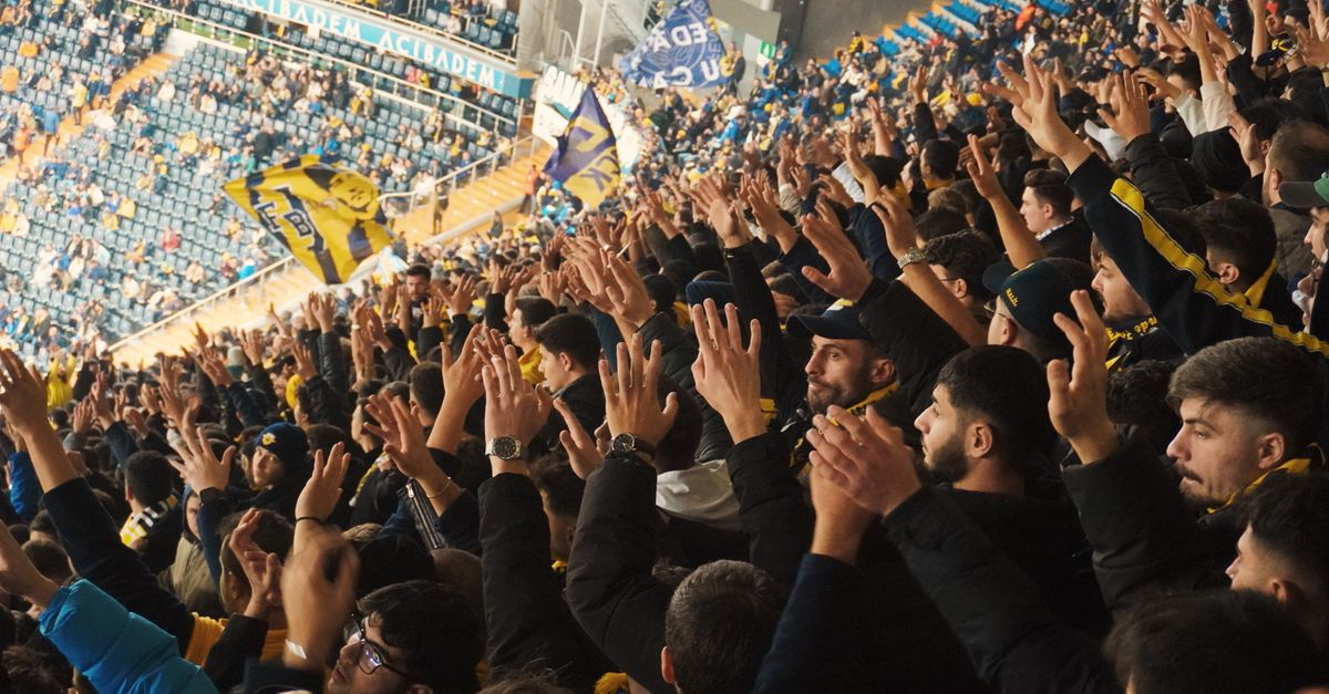 Energetic fans with raised hands in a stadium, supporting their soccer team with enthusiasm.