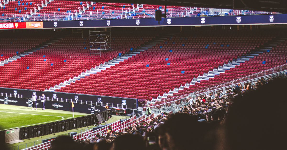 Panoramic view of stadium with empty red seats and crowd gathered for a live match.