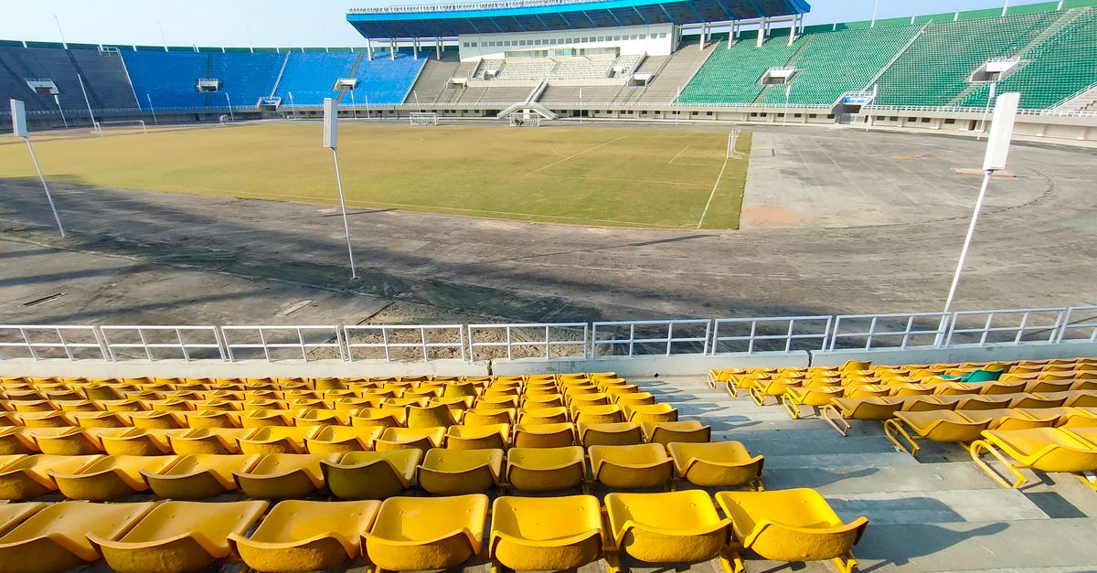 A wide shot of an empty stadium with colorful seating under bright daylight.