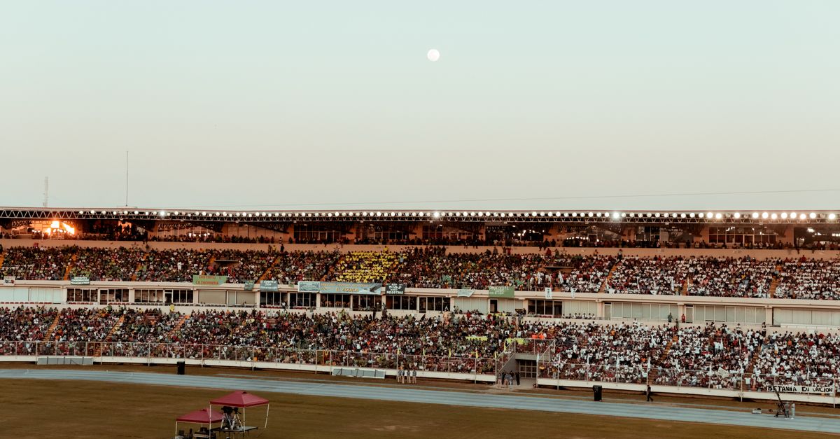 A bustling crowd fills the stadium under a clear evening sky, creating a vibrant atmosphere.