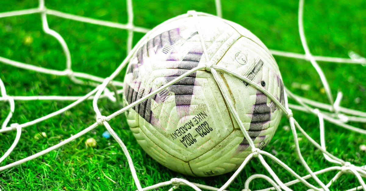 A close-up of a soccer ball caught in the net on a green grass field.